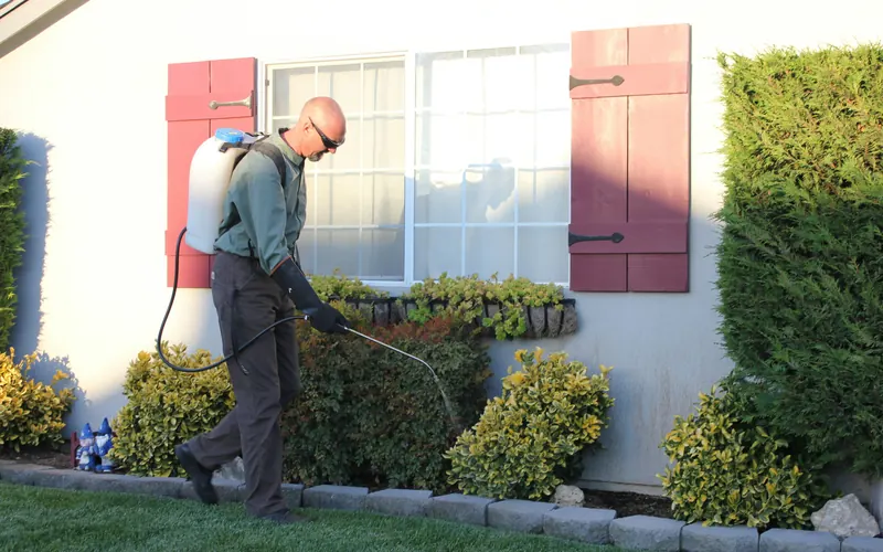A pest control technician spraying around the outside of a house