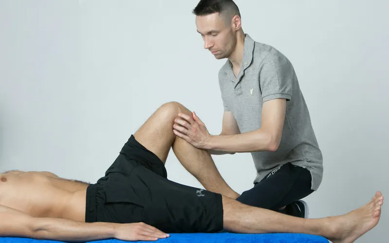 A physiotherapist assessing a patient's knee on a treatment table